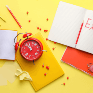Red alarm clock with notebooks and pins on table.