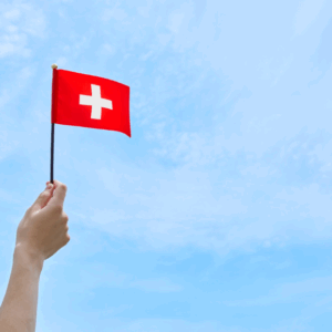 Hand waving Swiss flag against blue sky.