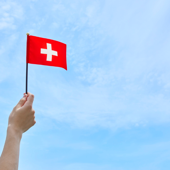 Hand waving Swiss flag against blue sky.
